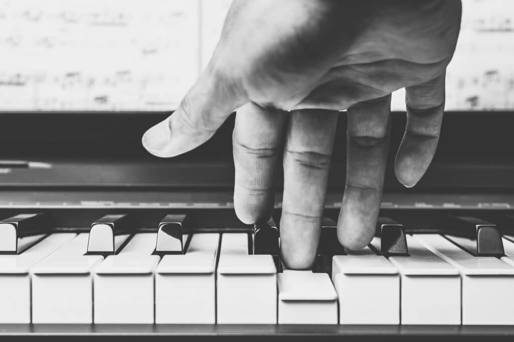 Gros plan en noir et blanc sur des doigts jouant du piano, action de presser les touches blanches.