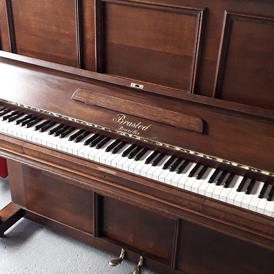 Piano droit Brasted Bruxelles en bois sombre, avec clavier complet noir et blanc et deux pédales en laiton. Aspect vintage.