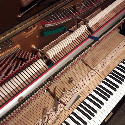 Mécanisme interne de piano à queue ouvert : cordes, marteaux, étouffoirs. Outils de réparation ou d'accordage sont posés sur l'action et le clavier.