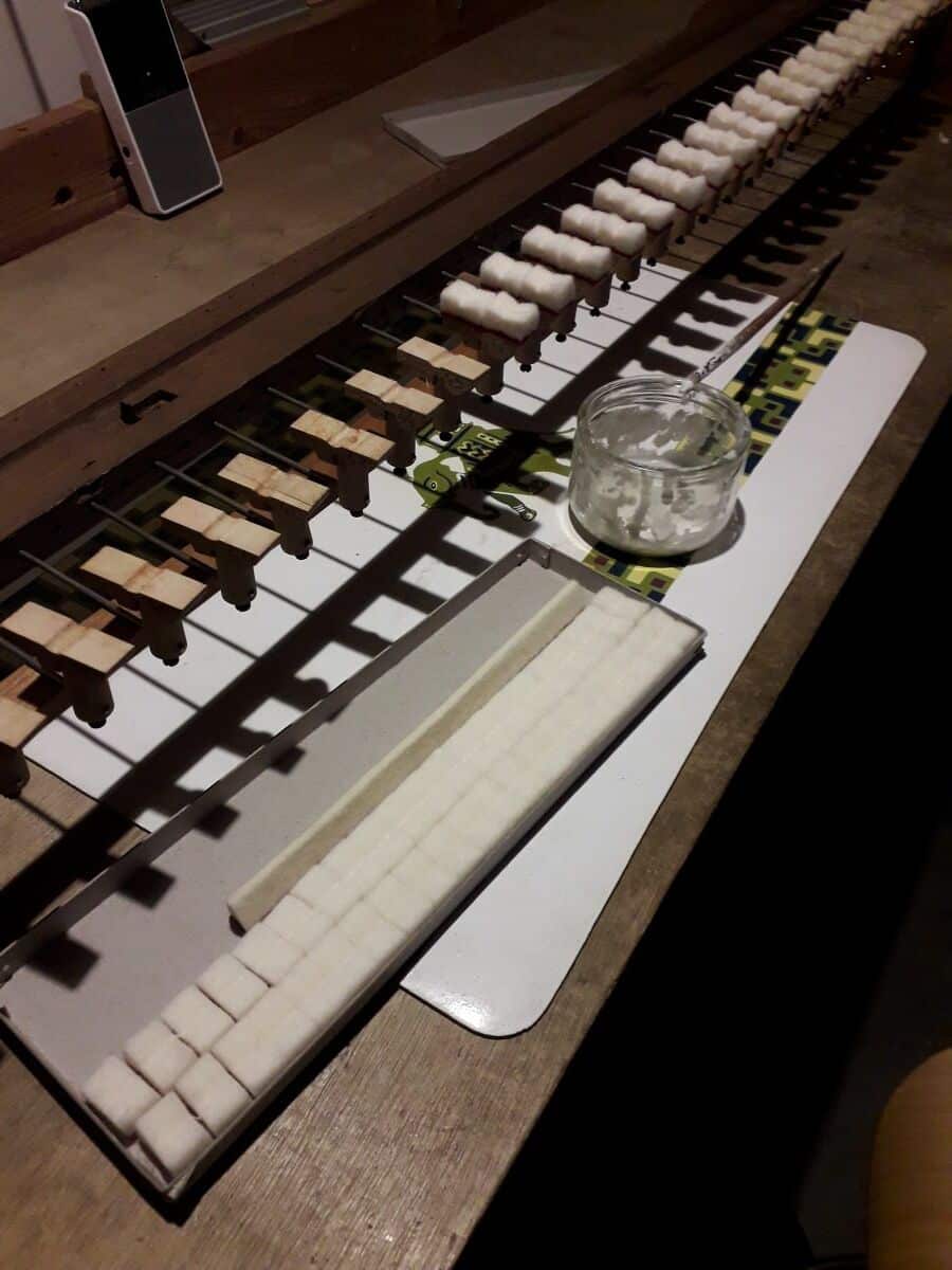Rangement créatif : Sucres, coton et réparation piano Sucres en cubes alignés, blocs de bois garnis de coton blanc, pot de colle et pinceau sur un établi. Préparation ou réparation minutieuse.