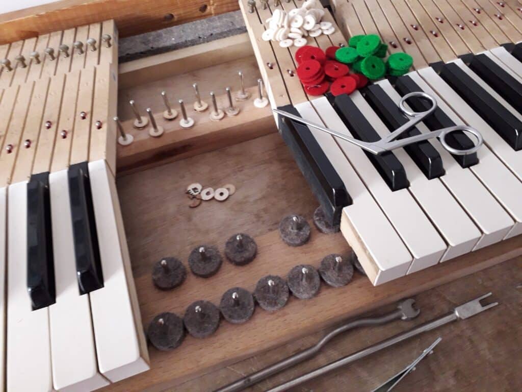 Clavier de piano ouvert pour réparation, avec touches noires et blanches. Divers feutres colorés (blancs, rouges, verts) et outils de réglage sont posés.