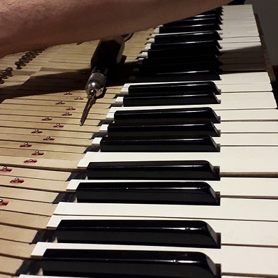 Main avec un tournevis ajustant la mécanique d'un piano. Clavier avec touches blanches et noires et structure interne en bois exposée.