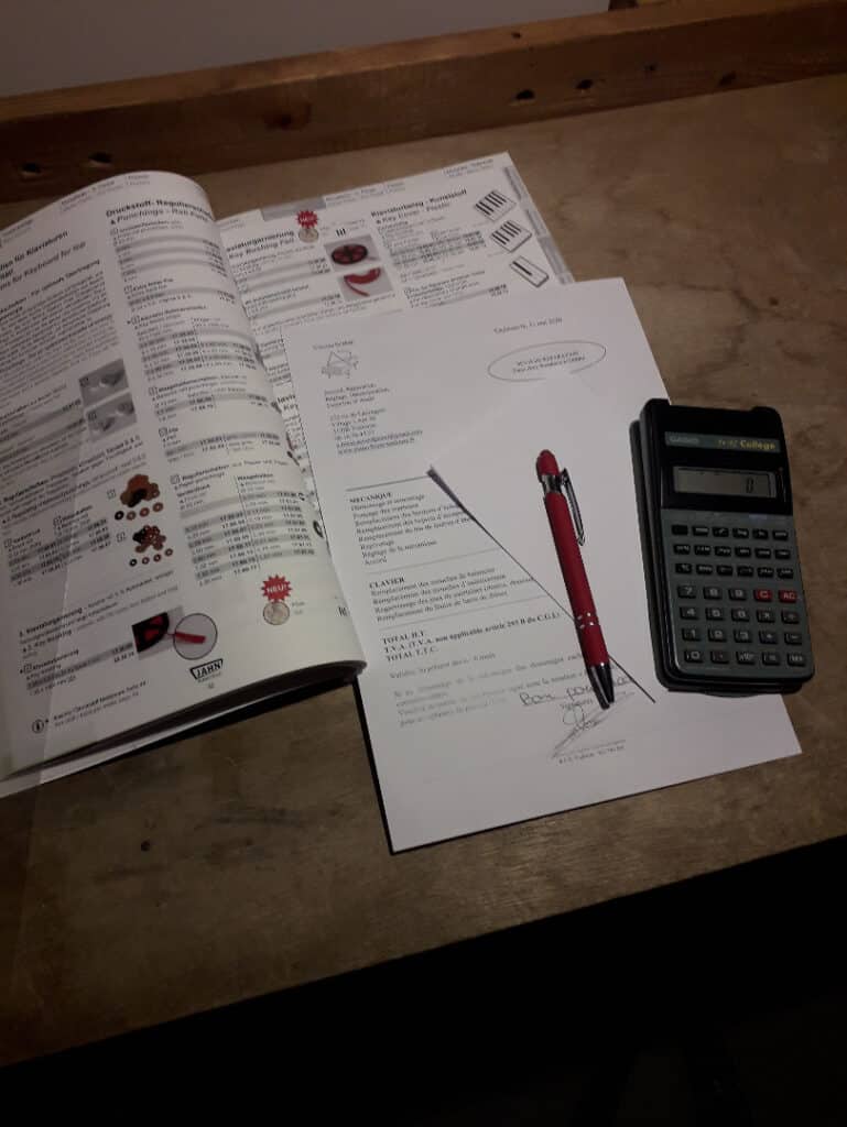 Catalogue pièces claviers, calculatrice et devis signé Catalogue de pièces détachées pour claviers, document signé, stylo rouge et calculatrice Casio fx-991 College sur table en bois.