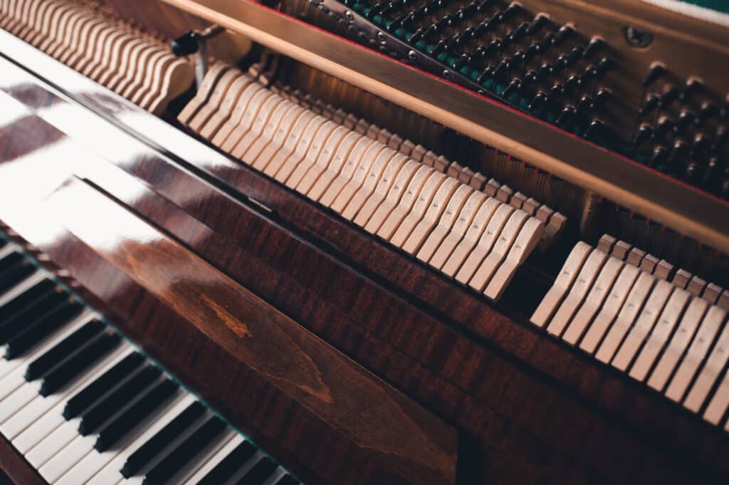 Vue rapprochée des marteaux de feutre et des touches blanches et noires d'un piano droit ouvert, bois sombre brillant.