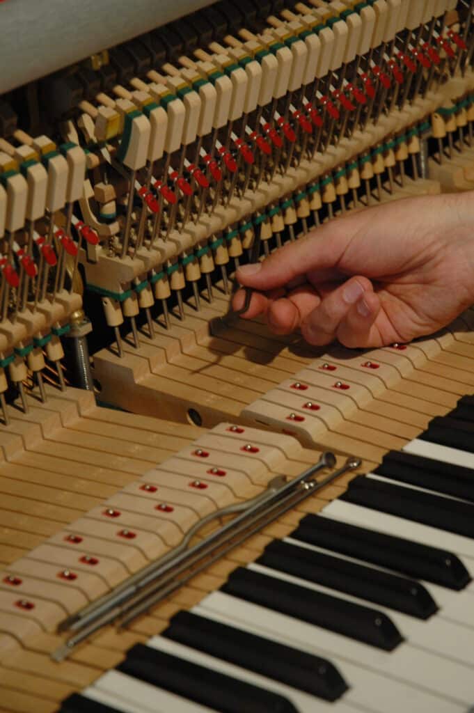 Réglage mécanique de piano : ajustement des marteaux Main d'un technicien ajustant les mécanismes internes d'un piano, près des marteaux et des touches visibles.